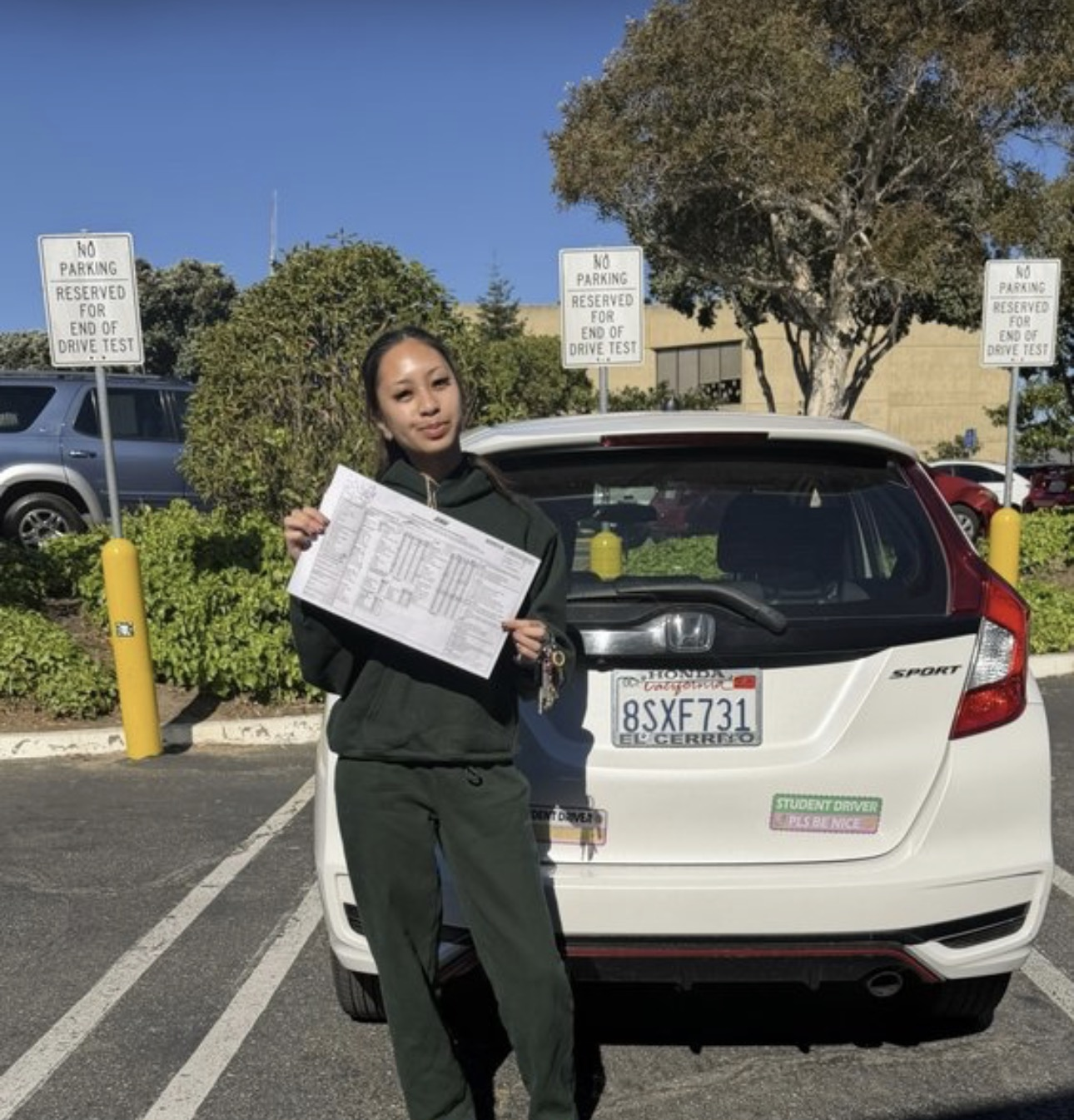 Student holding her driving test report in front of the training car