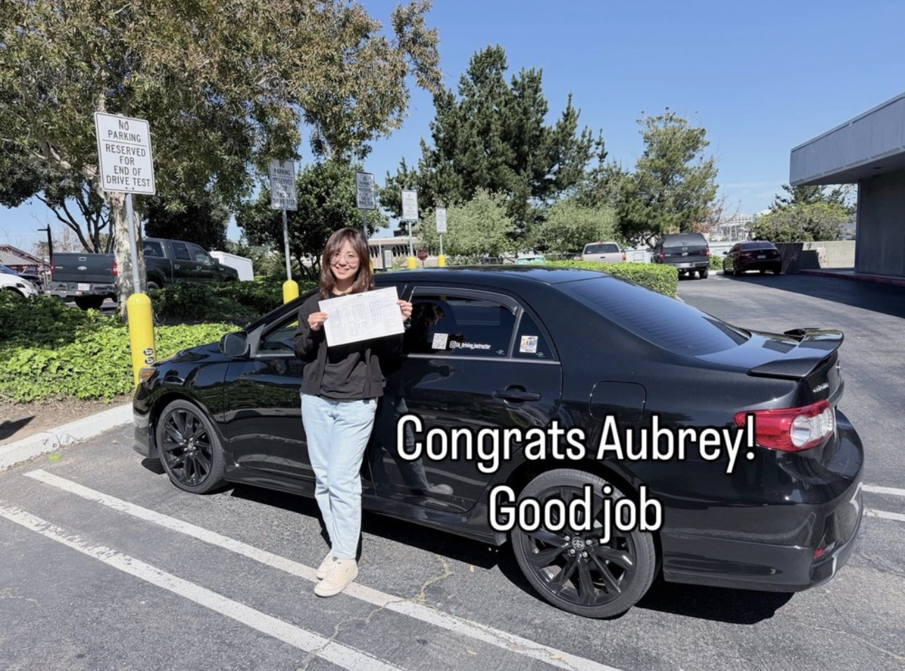Student celebrating her driving test pass next to the training car